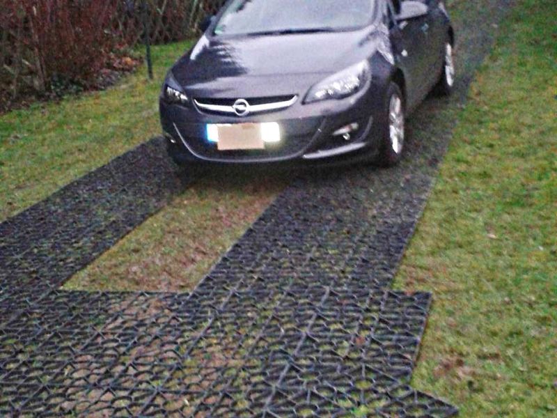 Ein Auto fährt über eine auf Rasen verlegte Fahrstraße aus Kunststoff-Rasengittern.