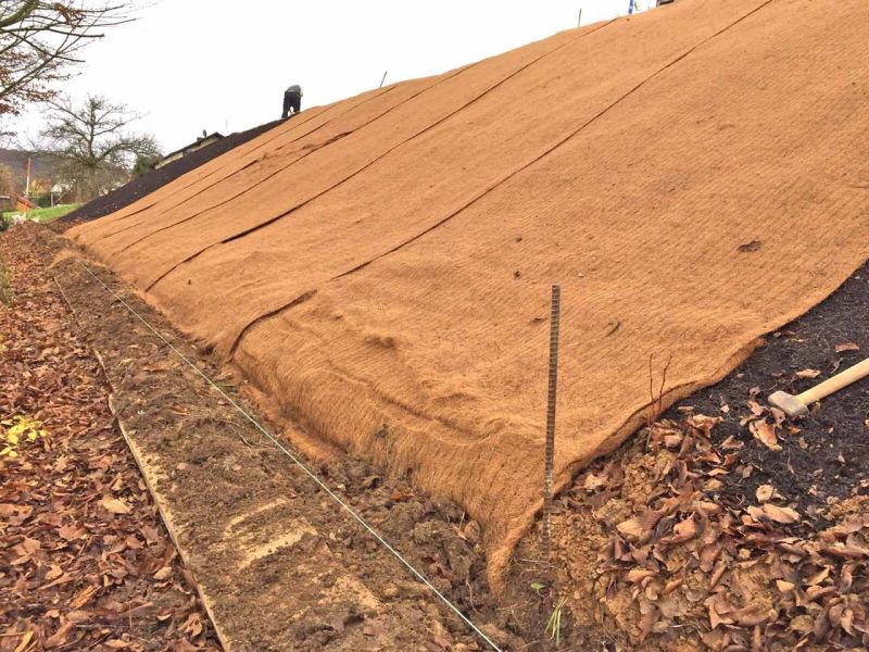 Verlegung einer Mulchmatte auf einer Böschung zur Stabilisierung des Hangs.