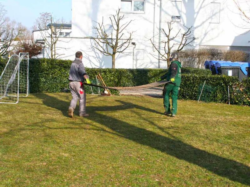 Zwei Arbeiter tragen eine Kunststoff-Fahrplatte für die Verlegung auf einer Baustelle bei Bagger- und Erdarbeiten