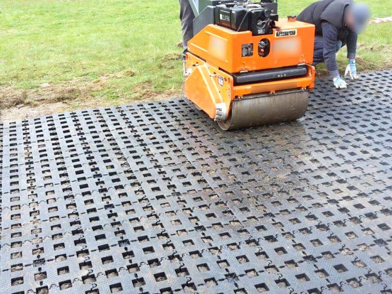 Eine kleine Walze wird zum Eindrücken der Rasengitterstein RGS35 in den Boden verwendet. Eine Person kniet daneben, um die Platte auszurichten.