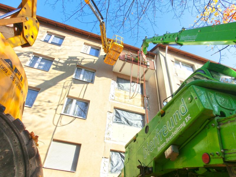 Teleskoplader und Arbeitsbühne arbeiten gleichzeitig an der Fassade eines Wohnhauses beim Rückbau eines Balkons.