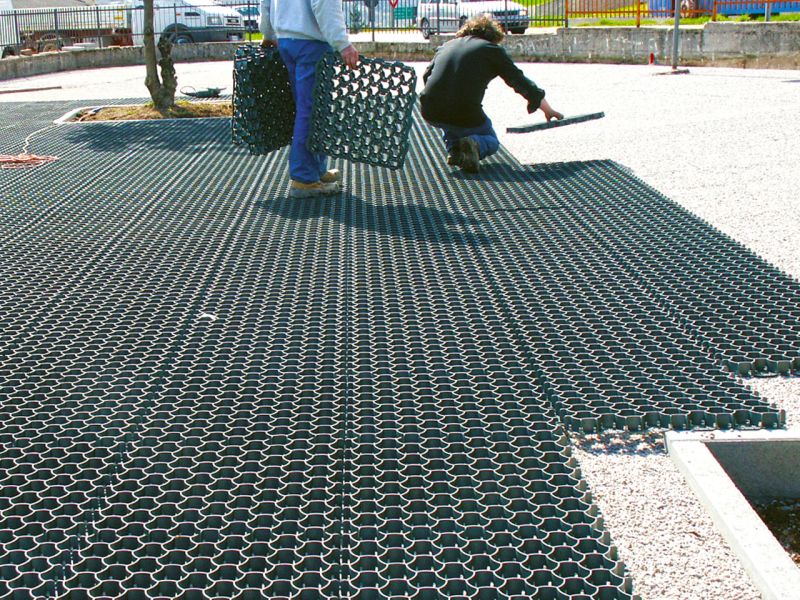 Arbeiter verlegen schwarze Kunststoffwaben als Unterbau für befahrbaren Rasen. eines Rasen mit der Rasenwabe RW40 für einen Parkplatz