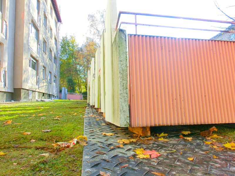 Mehrere abgetrennte Balkonelemente liegen geordnet auf stabiler Fläche im Grünbereich neben den Wohnhäusern.