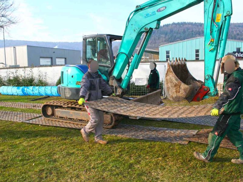Zwei Personen transportieren eine s:tek-Bodenschutzplatte zur Verlegung auf dem Rasen bei Bagger- und Erdarbeiten