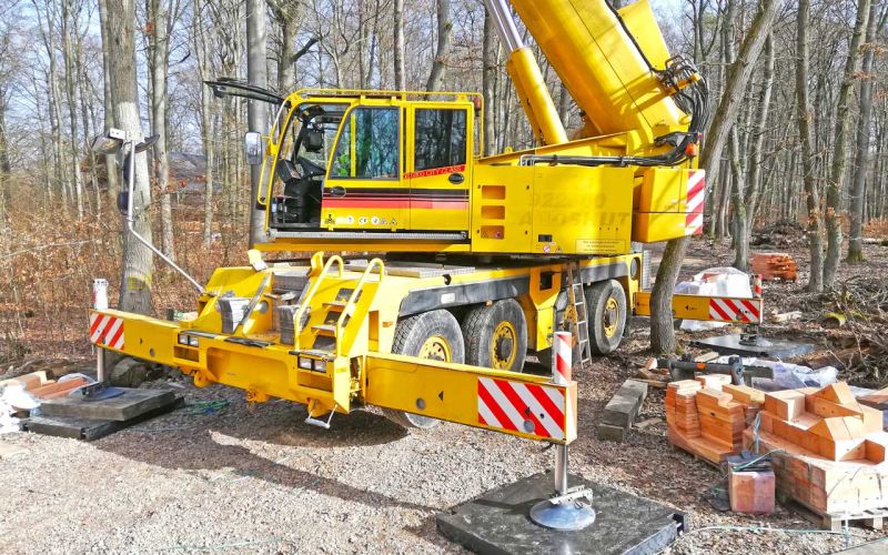 Mobiler Autokran mit ausgefahrenen Stützen auf Kranmatten aus Kunststoff im Waldgebiet