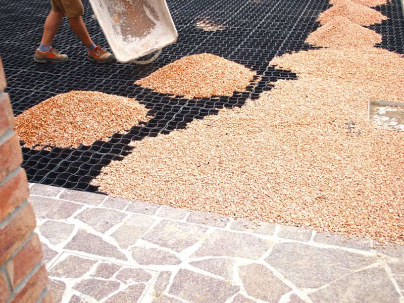 Arbeitskraft verteilt rötlichen Kies auf ausgelegten Gitterwaben.