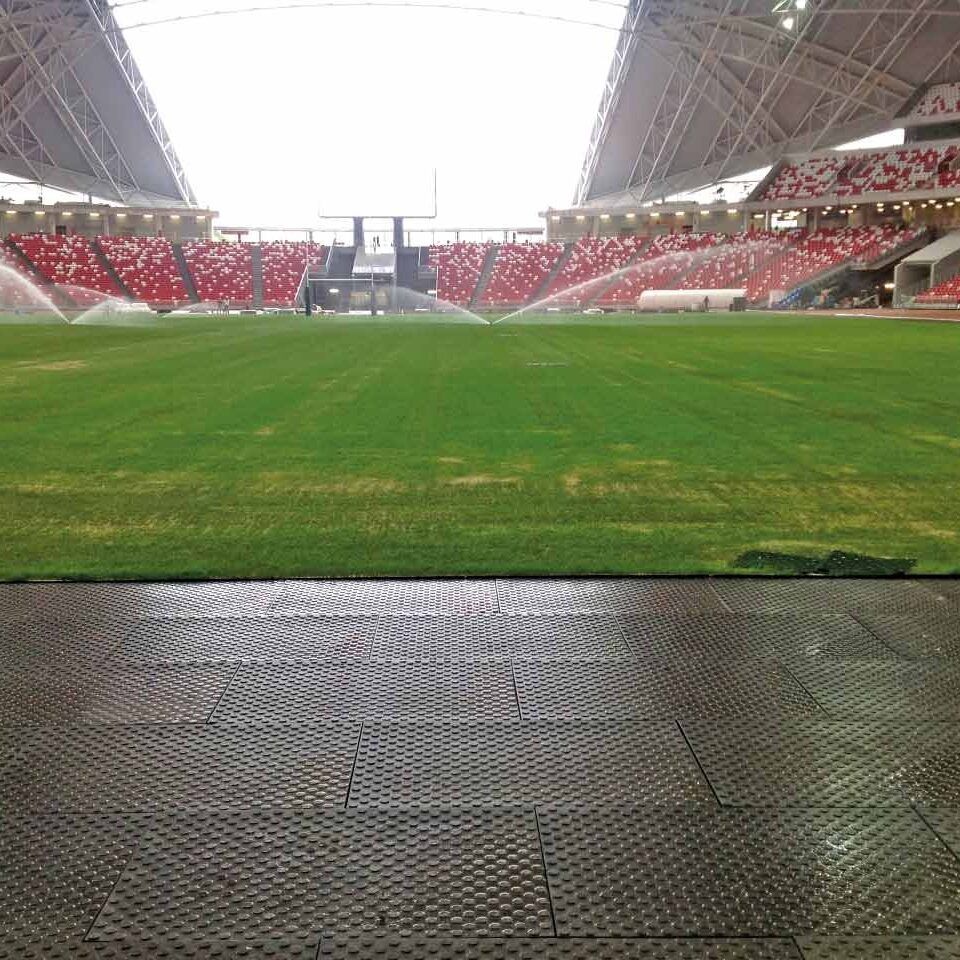 Blick auf den Rasen einen Stadions. Am Rand sind Bodenmatten verlegt. Im Hinergrund sieht man die Tribünen.