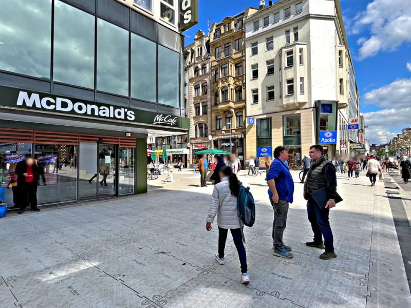 Personen gehen Shoppen in der Fußgängerzone. Es ist ein sonniger Tag. Geschäfte im Hintergrund.