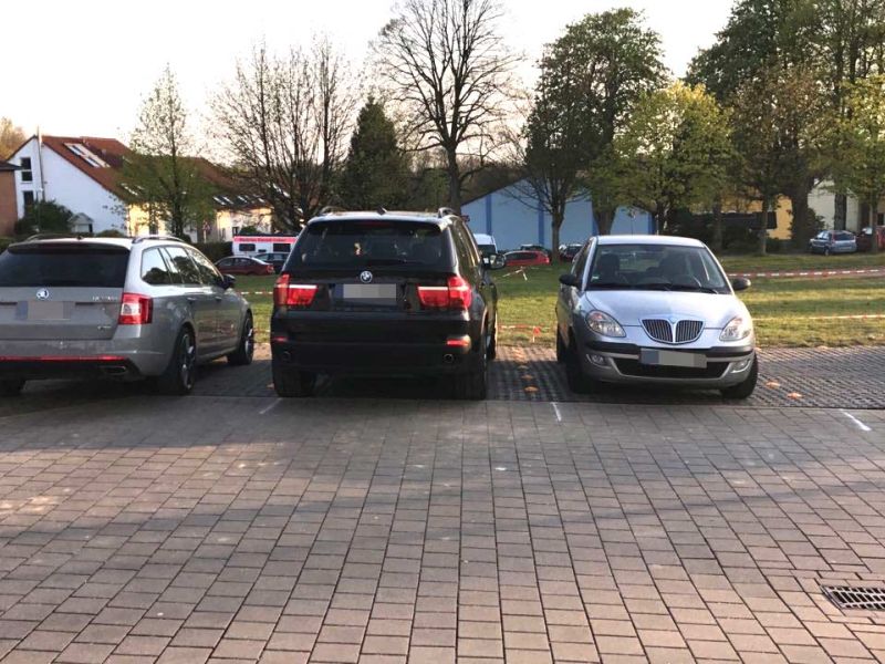 Fahrzeuge aus einem Parkplatz. Im Hintergrund sieht man Bäume und Gebäude.