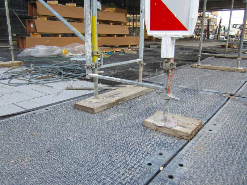 Nahaufnahme einer Bodenschutzmatte, die als stabile Unterlage für ein Gerüst auf einer Baustelle dient.