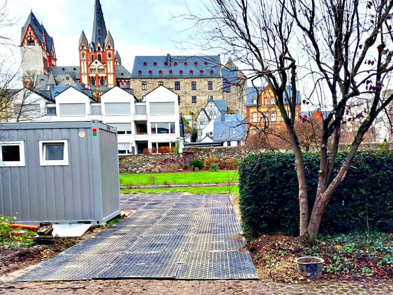 Eine mobile Baustraße aus Fahrplatten verlegt zwischen einem Baum und einem Container