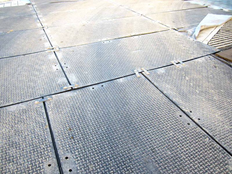 Mehrere Kunststoffplatten, die als Schutz für einen gepflasterten Untergrund auf einer Baustelle verlegt wurden. Die Platten sind miteinander verbunden und bieten eine robuste Abdeckung.