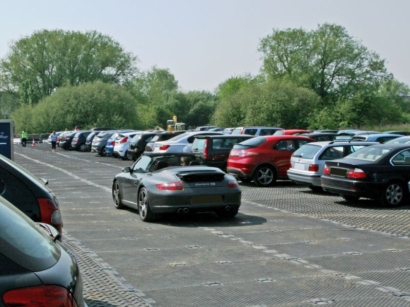 Temporärer Parkplatz für Veranstaltung mit geparkten Autos auf Bodenschutzplatten in natürlicher Umgebung.