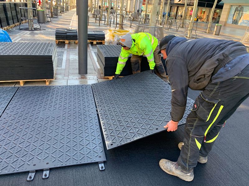 Zwei Personen verlegen x:tek46 Fahrplatten auf Gummimatten, um den gepflasterten Untergrund zu schützen.