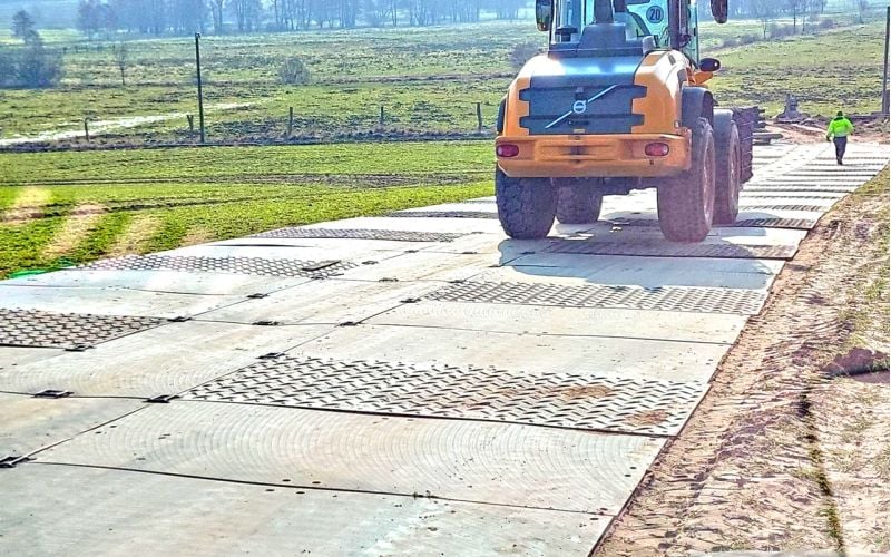 Ein Radlader fährt über eine mobile Baustraße aus Fahrplatten, die auf einer Wiese verlegt ist