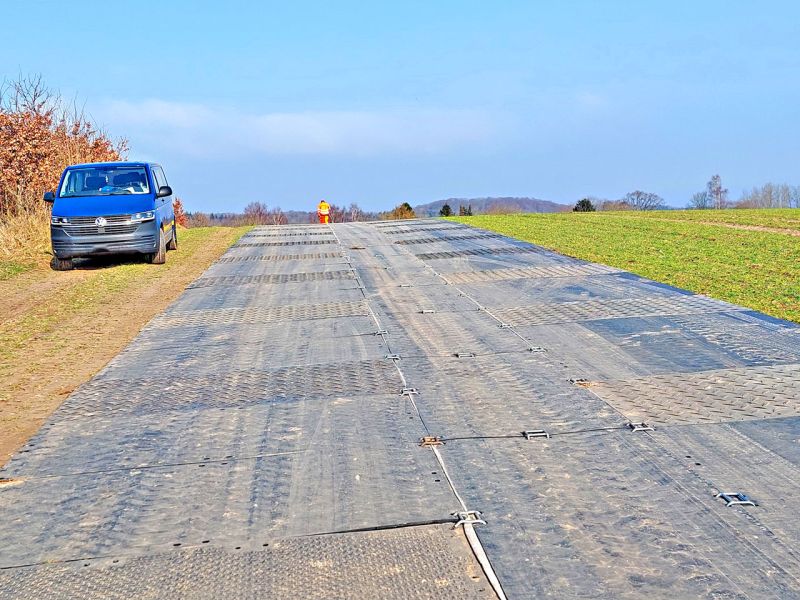 Auf einer Wiese liegen Fahrplatten, die so eine Straße bilden. Daneben steht ein blaues Fahrzeug.