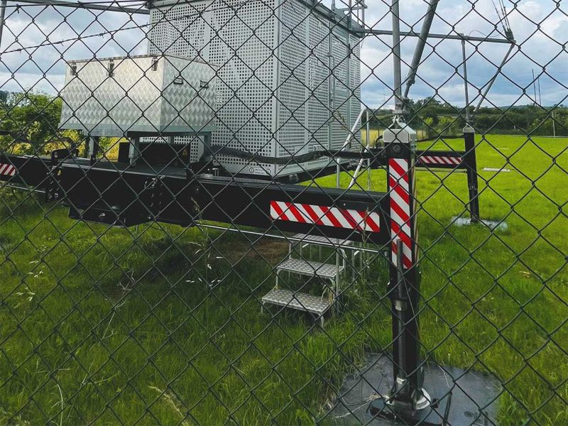 Ein Mobiler Radio Trailer hinter einem Zaun auf einer Wiese.