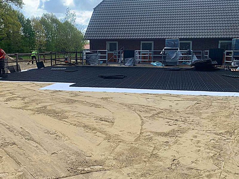Auf einer sandigen Fläche werden Trennvlies und Bodengitter verlegt zum Paddock befestigen