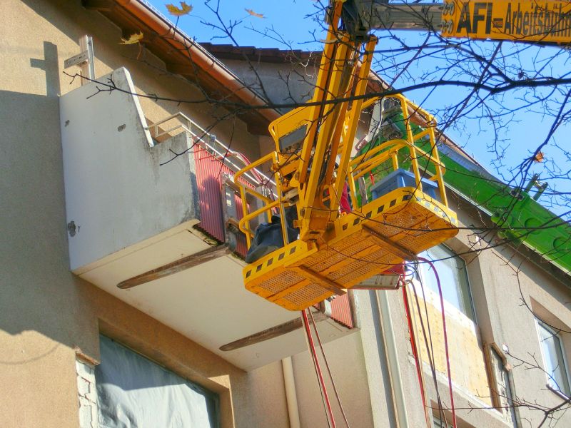 Arbeitsbühne steht direkt am Balkon eines Mehrfamilienhauses, um Bauteile sicher zu lösen und zu kontrollieren.