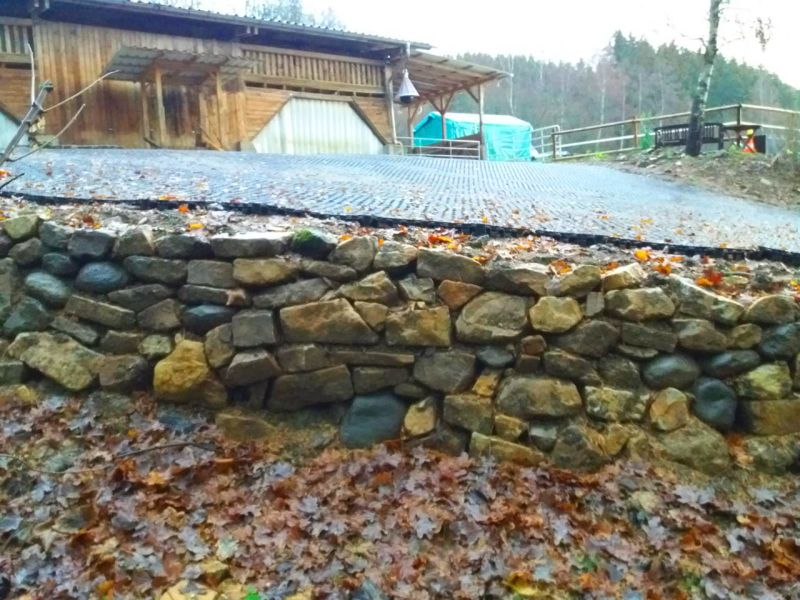 Stabile Natursteinmauer als Hangbefestigung in einem Pferdepaddock mit Bodenplatten.