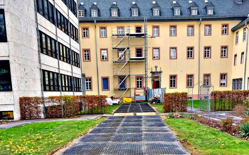 Fahrplatten als breiter Weg verlegt vor einem Gebäude. Vor dem Gebäude ist ein Gerüst aufgebaut.