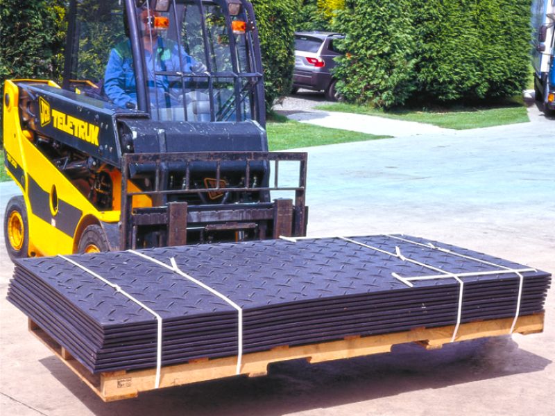 Gabelstapler transportiert gestapelte schwarze Platten auf einer Palette im Außenbereich.