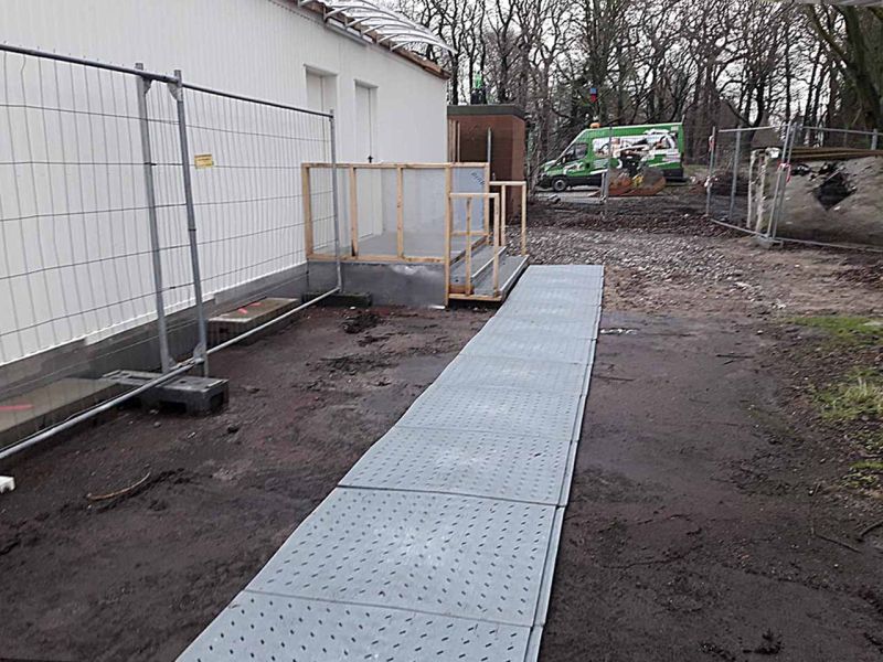 Ein temporärer Gehweg aus Bodenmatten vor einem Raumcontainer