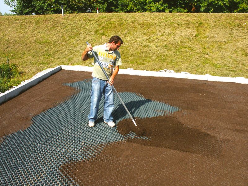 Arbeiter verteilt Erde über verlegte Rasenwaben zur Befüllung und Vorbereitung der Rasensaat.