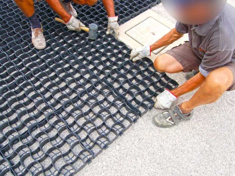 Galabauer verlegen schwarze Bodengitter zur Stabilisierung der Fläche.