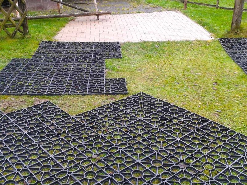 Auf einer Wiese wurden Rasengitter verlegt. Im Hintergrund ist ein Holzzaun und ein gepflasterter Weg zu sehen.