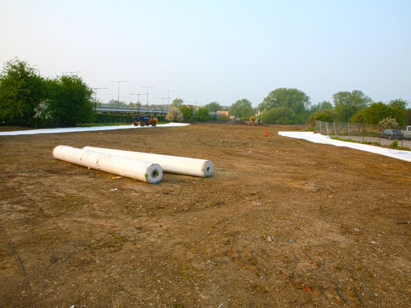 Große Erdfläche mit ausgerolltem Geotextil und Materialrollen zur Flächenvorbereitung.