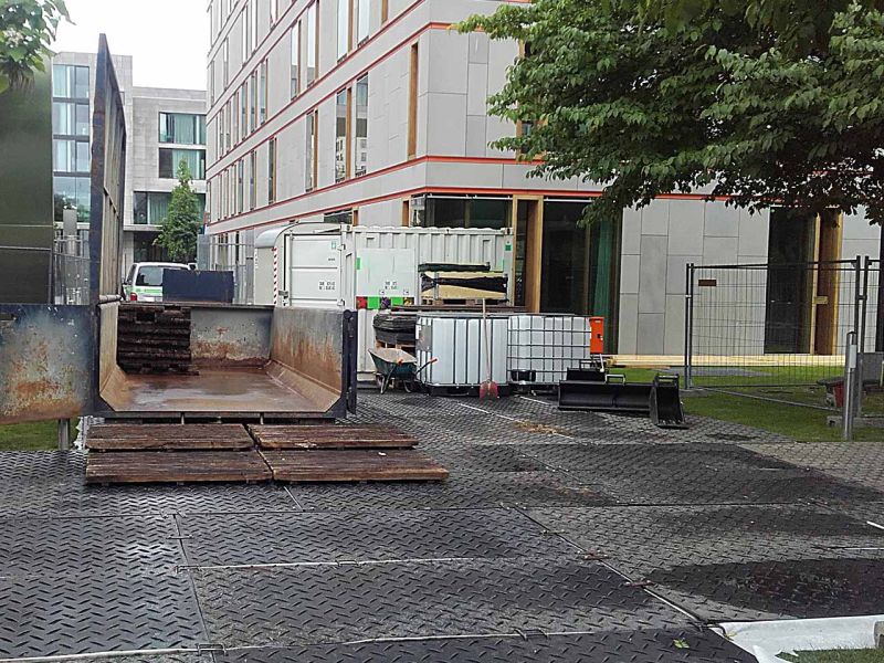 Eine Stellfläche aus Bodenschutzplatten vor einem Gebäude. Darauf steht ein Container. Vor dem Gebäude steht ein Baum.