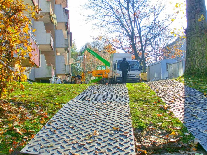 Zwei stabile Mattenwege führen über den Rasen zur Rückbaustelle zwischen Wohnhäusern.