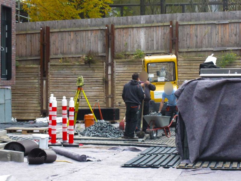 Arbeiterteam und Minibagger bei Vorbereitungen zur Dachbegrünung auf geschützter Fläche