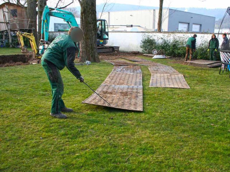 Arbeiter legen die s:tek Bodenschutzplatten aus, um eine Baustellenzufahrt über den Rasen zu schaffen.