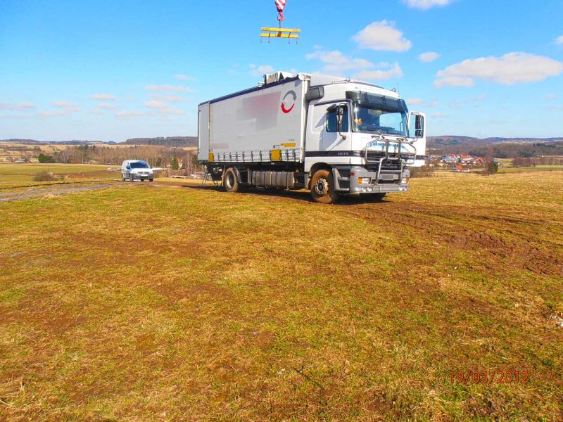 Blick auf Technikcontainer innerhalb Zaun, Kranarbeit mit Bodenschutzplatten im Einsatz