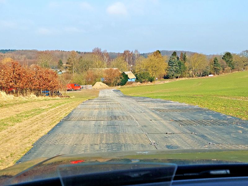 Eine mobile Baustraße aus Bodenschutzplatten auf einer Wiese. Im Hintergrund ist ein Wald zu sehen.
