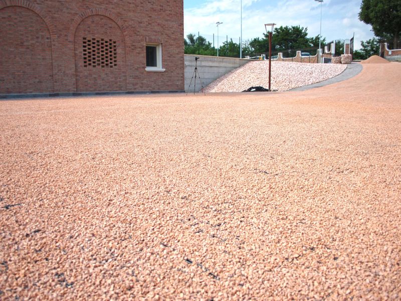 Fertig verdichtete rötliche Kiesfläche vor mediterranem Gebäude.