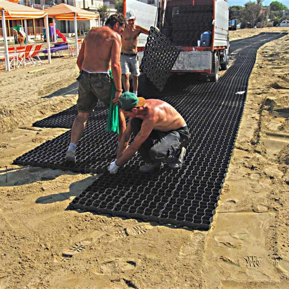 Mehrere Bauarbeiter verlegen das Boidengitter BG30/BG50 auf einer Sandfläche