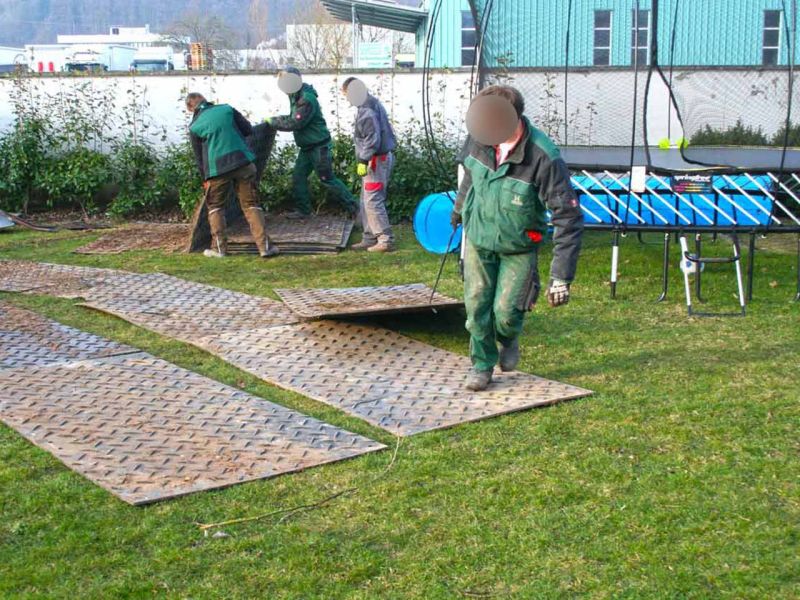 Arbeiter zieht eine Bodenschutzplatte mit einem Handhaken über den Rasen.