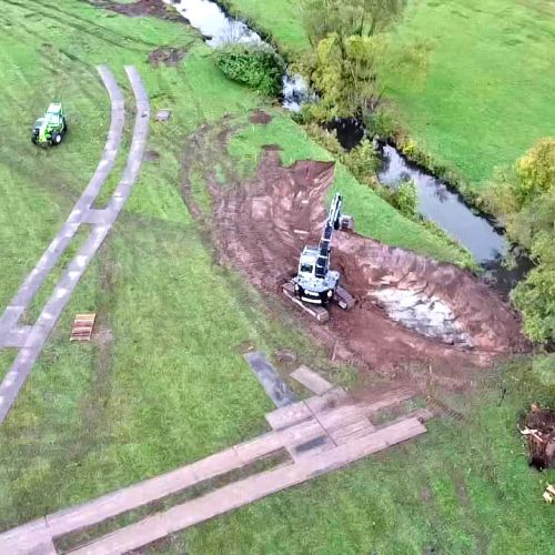 Langlebige Fahrplatten als mobile Baustraße schützen Waldboden & Wiesen bei Bauarbeiten zur Renaturierung eines Flussbetts.