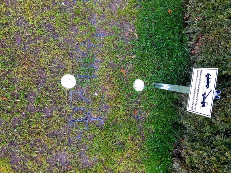 Ein Rasengitter-Parkplatz mit weißen Markierungen. Rechts ein Schild mit Auto-Symbol und Abschlepphinweis. Der Rasen wächst durch die Gitter hindurch.