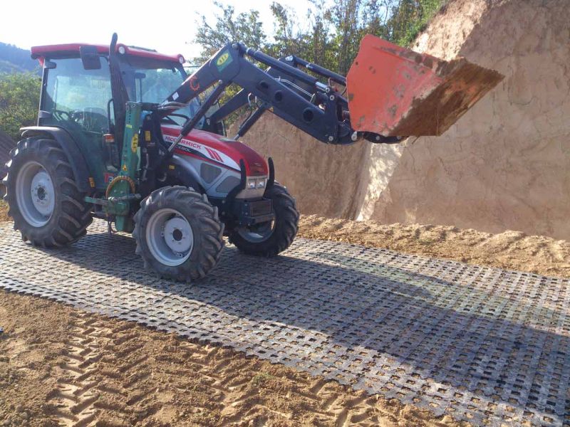 Traktor fährt auf Weg aus Rasengittersteinen. Im Hintergrund ist ein sandiger Hügel.