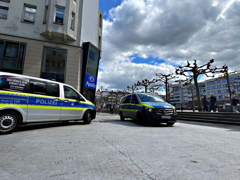 Zwei Polizeifahrzeuge fahren über Bodenschutzplatten. Personen treffen sich in einer Parkanlage.