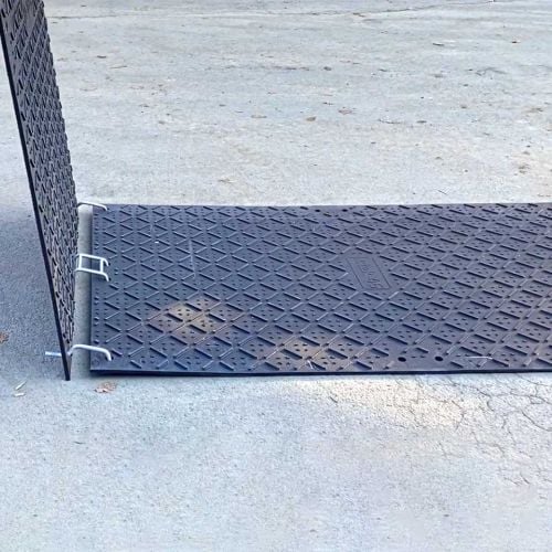Auf einer Straße werden Bodenschutzplaten verlegt. Die Fahrplatten werden mit Verbindern aus Stahl verbunden.