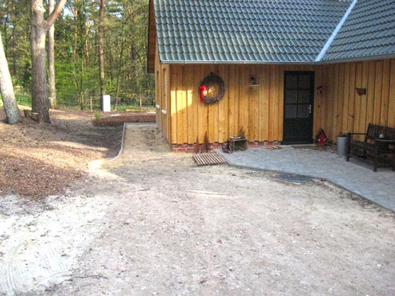 Holzhaus inmitten eines Waldes mit einer angrenzenden Kiesfläche und einer Terrasse aus Naturstein.