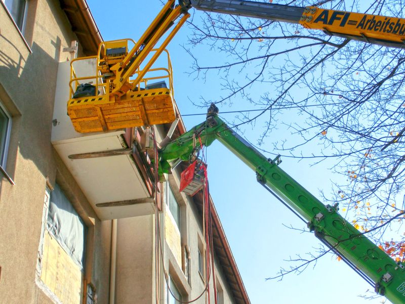 Zwei Hubgeräte greifen an einer Balkonplatte an, um sie kontrolliert zu lösen. Arbeiten finden nah am Gebäude statt.
