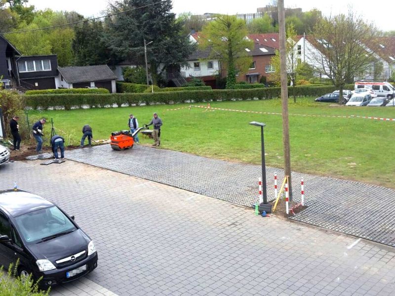 Neben einer gepflasterten Straße wird auf einem Rasen ein Parkplatz angelegt