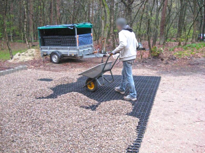 Arbeiter verteilt mit einer Schubkarre Kies auf einem zuvor verlegten Bodengitter zur Stabilisierung der Fläche.