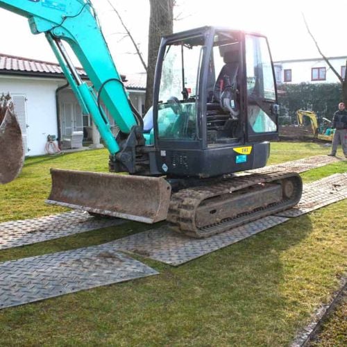 Ein Bagger fährt über eine mobile Fahrstraße aus Bodenschutzplatten, um den Rasen zu schützen.